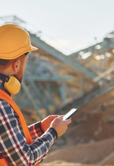 With yellow headphones on neck. Construction worker in uniform is on the quarry.